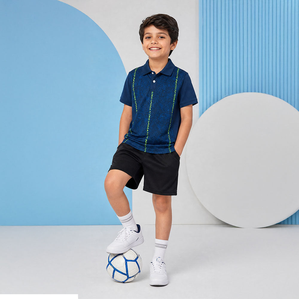 Kids' polo sports jersey in navy blue with lime vertical accents, worn by a child in black shorts resting one foot on a football in a studio.