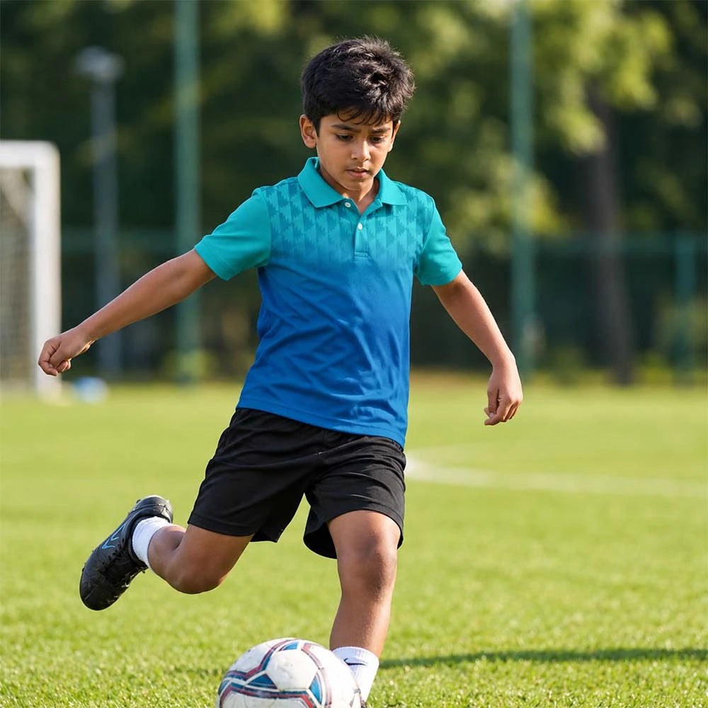 Child wearing the turquoise-to-blue gradient with a geometric shoulder pattern polo jersey with black shorts, kicking a football.